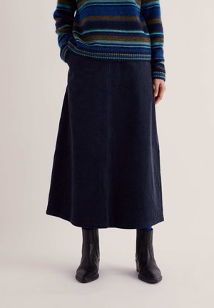 Person wearing a navy blue corduroy midi skirt, black ankle boots, and a striped blue, green, and brown sweater with hands in pockets.