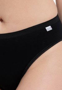 Schwarze Baumwollbikini-Unterwäsche mit glatter Textur, elastischem Bund und einem kleinen Stoffetikett auf der Vorderseite, das ein schlichtes Design bietet.