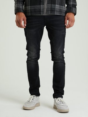 Jeans in denim nero con una vestibilità slim, caratterizzati da una leggera sbiaditura e una texture liscia. Abbinati a sneaker grigie chiare e una camicia a quadri.