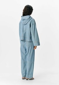 Hellesblaues Denim-Outfit bestehend aus einem cropped Hoodie und weit geschnittenen Hosen. Der Stoff hat eine glatte Textur mit sichtbaren Nähdetails.