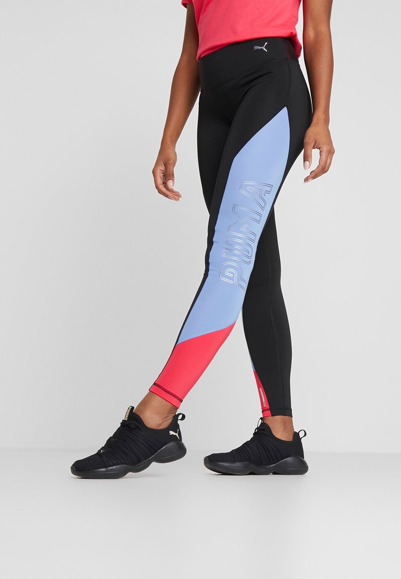 Leggings negros con acentos en azul claro y rojo, que presentan un destacado logo de "PUMA", combinados con zapatillas deportivas negras.