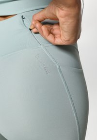 High-waisted, light mint athletic leggings with a side pocket and seamless design. Smooth texture, reinforced stitching, and small branding detail.