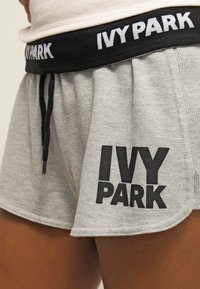 Shorts deportivos grises con el logo negro "IVY PARK" en la pierna izquierda y una cinturilla negra a juego con el texto blanco "IVY PARK", llevados por una persona.