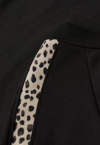 Svart tyg med en slät textur, med en sidopanel i tan, prydd med ett leopardmönster i mörkbruna och svarta fläckar.