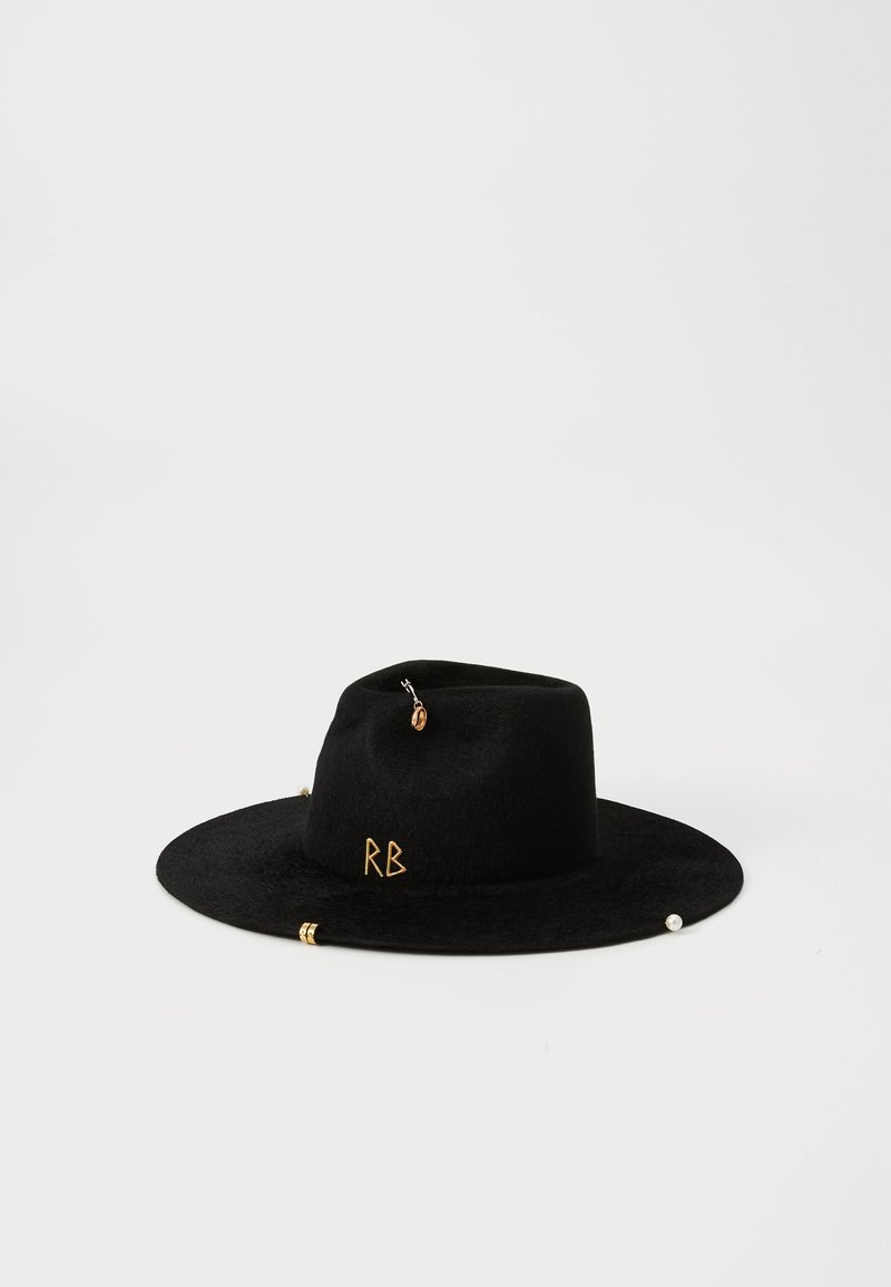 Μαύρο φέλτ φορεμά με φαρδύ γείσο, που διαθέτει μεταλλικά στοιχεία και τα αρχικά "RB" σε χρυσό. Σημαντικά διακοσμητικά στοιχεία περιλαμβάνουν μια πέρλα και διάφορες γοητείες.