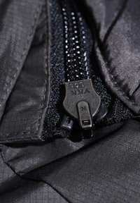 Czarny zamek błyskawiczny z logo YKK, kontrastujący siateczkowy materiał, przeszyte krawędzie oraz elegancka, gładka faktura na ciemniejszym tle.