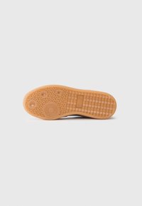 Talpa pantofului are o suprafață din cauciuc texturat de culoare maro deschis, cu modele circulare și hexagonale, precum și un imprimeu de brand.