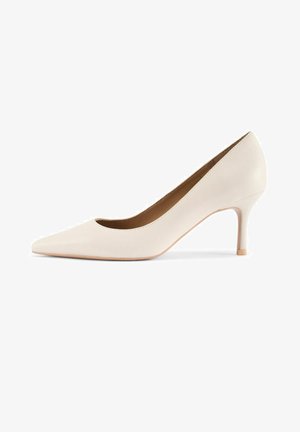 Beżowy damski szpiczasty czółenek ze skóry z średniej wysokości smukłym obcasem i gładkim wykończeniem, przedstawiony z boku na białym tle.