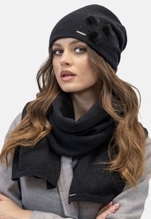 Berretto di lana nera con pompon decorativi e perline. Abbinato a una sciarpa nera coordinata, entrambi con una texture morbida e un design casual.