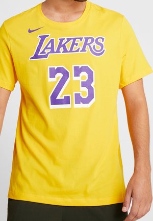 Mężczyzna w żółtej koszulce Lakers z fioletowym numerem 23 i logo Nike na piersi, pokazany od szyi do bioder.