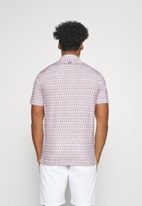 Chemise à manches courtes en tissu blanc avec un motif répétitif de flamants roses rouges, dotée d'un col montant et d'une texture lisse.