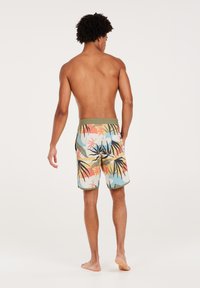 Shorts de bain pour hommes avec une taille verte. Le tissu présente un motif tropical coloré avec des feuilles dans des teintes rouge, jaune et bleue.