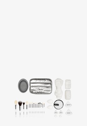Ensemble de différents pinceaux de maquillage, éponges, disques de coton et un sac à maquillage argenté, tous soigneusement disposés sur un fond blanc.