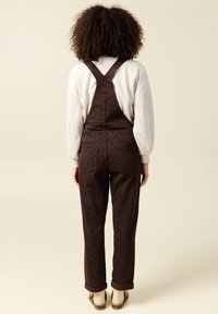 Bruna overall med leopardmönster, justerbara axelremmar, figursydd midja och tapered ben, i kombination med en ljusgrå sweatshirt.