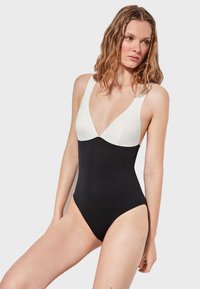 Bañador de una pieza con escote pronunciado, que presenta una parte inferior negra y una parte superior blanca, hecho de una tela suave. Diseño sencillo, sin patrones.