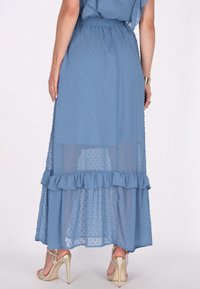 Gonna maxi azzurro chiaro e trasparente con texture a pois. Presenta un orlo arricciato e una vita elastica. Abbinata a sandali dorati con tacco alto.