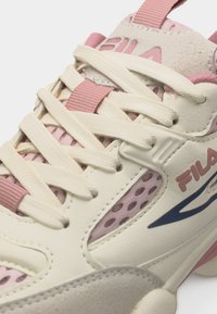 Κοντινό πλάνο σε αθλητικό παπούτσι FILA σε κρεμ και ροζ αποχρώσεις με πάνελ από δίχτυ, κρεμ κορδόνια και λεπτομέρειες στη σόλα με υφή.