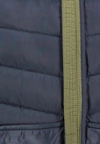 Giacca puffer blu navy con una cerniera in tessuto verde oliva. Cuciture visibili lungo le cuciture, che mettono in evidenza le sezioni imbottite per l'isolamento.