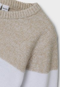 Gebreide trui met een beige en witte kleurblokontwerp. Heeft een geribbelde halslijn en een textuurstof met een zachte, geweven uitstraling.