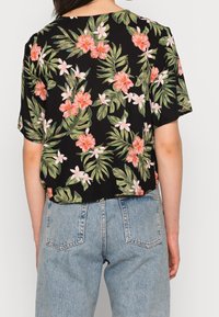 Schwarzes Kurzarmhemd mit pinkem und weißem Blumenmuster, das grüne Blätter aufweist; lockere Passform mit Rundhalsausschnitt, kombiniert mit hellblauen Jeans.