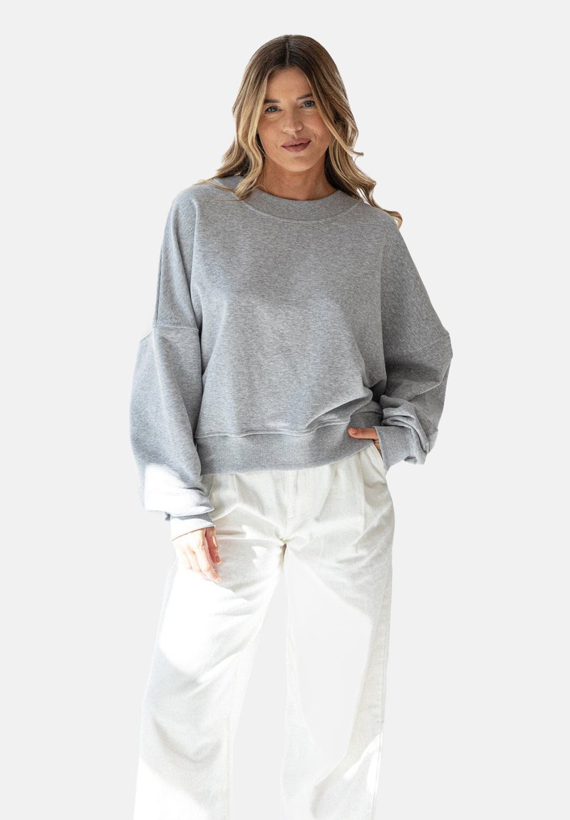 Szary, oversize'owy sweter z okrągłym dekoltem i opuszczonymi ramionami, w zestawie z jasnymi, szerokimi spodniami. Miękka tkanina i luźny krój.