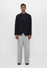 Zwarte blazer met twee knopen, notch-lapels en voorzakken, gecombineerd met lichtgrijze wijde broek. Eenvoudig, op maat gemaakt ontwerp.