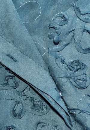 Blauwe textuurstof met gestikte en versleten bloemmotieven en een stoffen knoop op een gelaagde kledingoppervlak.