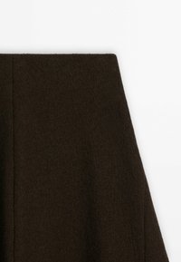 Tissu en laine brun foncé à surface texturée, découpé en forme rectangulaire inclinée sur fond blanc.