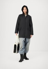 Veste à capuche noire avec une fermeture éclair sur le devant, poches latérales, associée à un jean large bleu clair, des bottines à talons noires et un sac en fourrure.