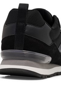 Vue arrière d'une basket noire avec une tige en mesh, des détails en daim, une languette de traction et une semelle rembourrée grise et blanche.