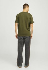 Olivenfarvet kortærmet T-shirt med rund hals, glat tekstur og afslappet pasform, båret med mørkegrå vide bukser.