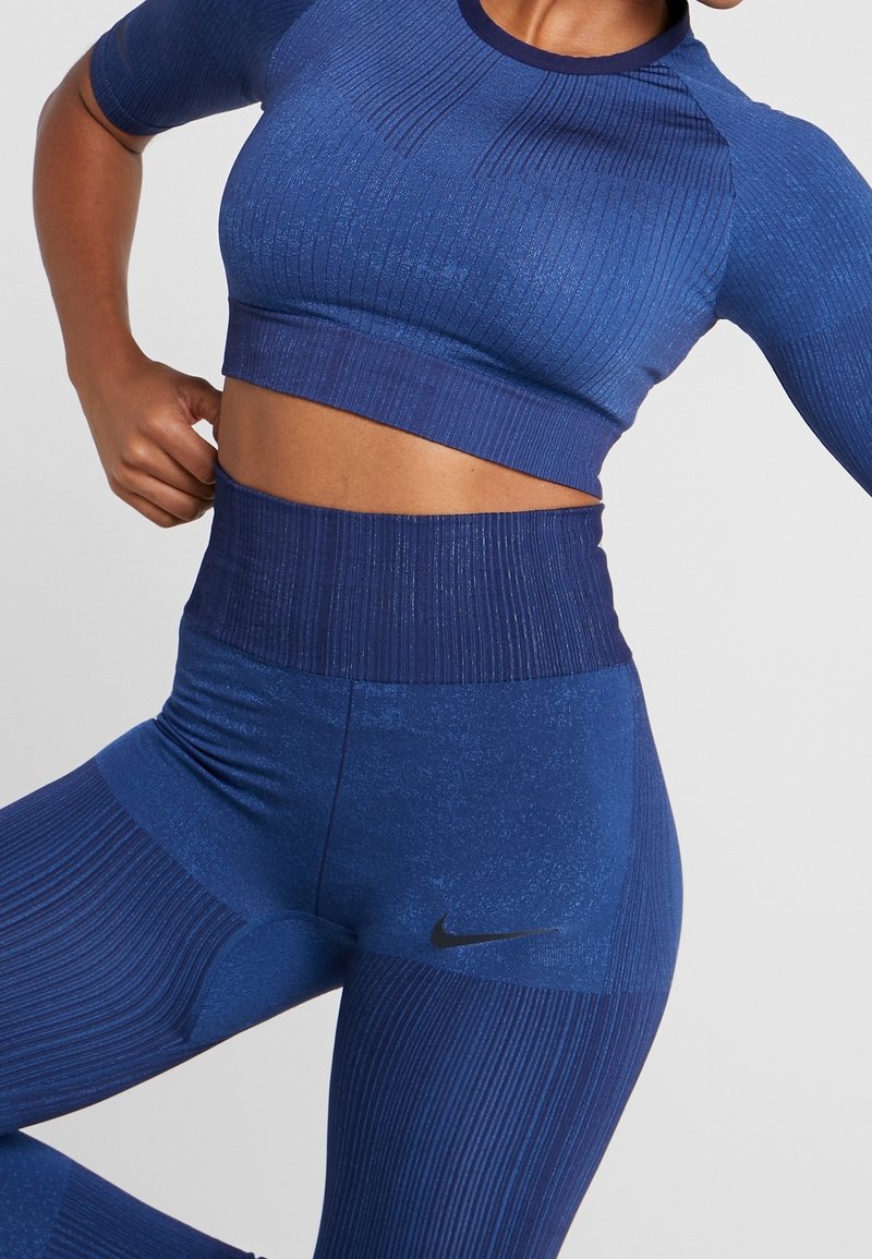 Modrý sportovní cropped top a legíny s vysokým pasem vyrobené z texturované, žebrované látky. Obsahuje jemný lesk a černé logo Nike na legínách.