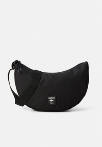 Musta Lacoste-laukku, jossa on puolikuun muotoinen rakenne ja teksturoidusta nailonista valmistettu. Siinä on olkahihna ja musta, valkoisin tekstillä varustettu brändätty etiketti.
