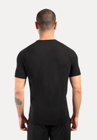 Camiseta ajustada de manga corta negra hecha de tejido suave, con cuello redondo y mangas raglán. Diseño minimalista sin logotipos visibles.