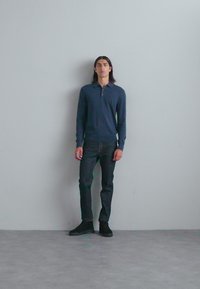 Dark blue long-sleeve polo shirt, slim-fit black jeans, and black sneakers. Simple design, smooth texture, fitted silhouette.