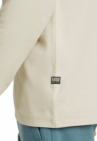 Light beige textured top with a G-Star tag on the hem, featuring a relaxed fit and ribbed detailing along the seams.