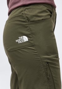 Κοντινό πλάνο ατόμου που φοράει παντελόνια The North Face σε χακί χρώμα με πίσω τσέπη με καπάκι και πλαϊνή τσέπη με φερμουάρ.