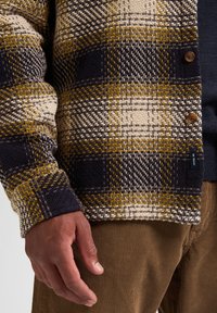 Gekapte wollen cardigan in marineblauw, beige en mosterd, met een gestructureerd patroon, voorzien van bruine knopen en een geribbelde kraag.