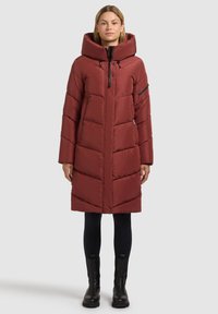 Piumino rosso con collo alto e cappuccio, presenta una cerniera frontale e tasche laterali. Il tessuto ha una texture liscia ed è imbottito.