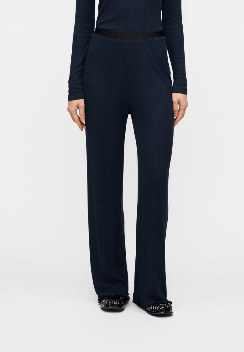 Παντελόνι σε ναυτικό μπλε με φαρδιά πόδια, κατασκευασμένο από απαλό ύφασμα με ομαλή υφή, διαθέτει ελαστική μέση και συνοδεύεται από εφαρμοστό μακρυμάνικο τοπ.