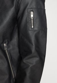 Schwarze Lederjacke mit strukturiertem Finish, die über einen Reißverschluss an den Taschen an den Ärmeln und an der Seite verfügt und somit funktionale Details zum Design hinzufügt.