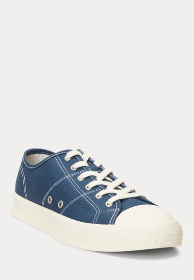 Blå canvas sneakers med vit gummisula, rund tå och kontrasterande sömmar. Har metallögon och platta snören.