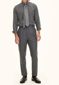 Grijze overhemdbloes met een das, gecombineerd met grijze geplooide broek. De outfit heeft een fijne textuur en een aansluitend ontwerp. Zwarte dresschoenen.