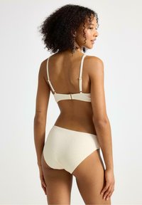 Krämfärgad bikini med en strukturerad, bikakestruktur; justerbara axelband och ett spänne bak; högmidjad underdel.