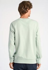 Vaalean mintunvihreä collegepaita, jossa on pyöreä kaula-aukko, pitkät hihat ja resorit. Pehmeä kangas ja rento leikkaus ilman näkyviä kuvioita tai varusteita.