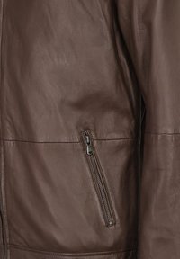 Braune Lederjacke mit glatter Textur, einer Reißverschlusstasche auf der linken Seite und einem klaren, minimalistischen Design.