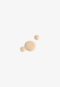 Liquide beige avec une texture lisse, présentant deux gouttes, l'une plus grande et l'autre plus petite, sur un fond blanc uni.