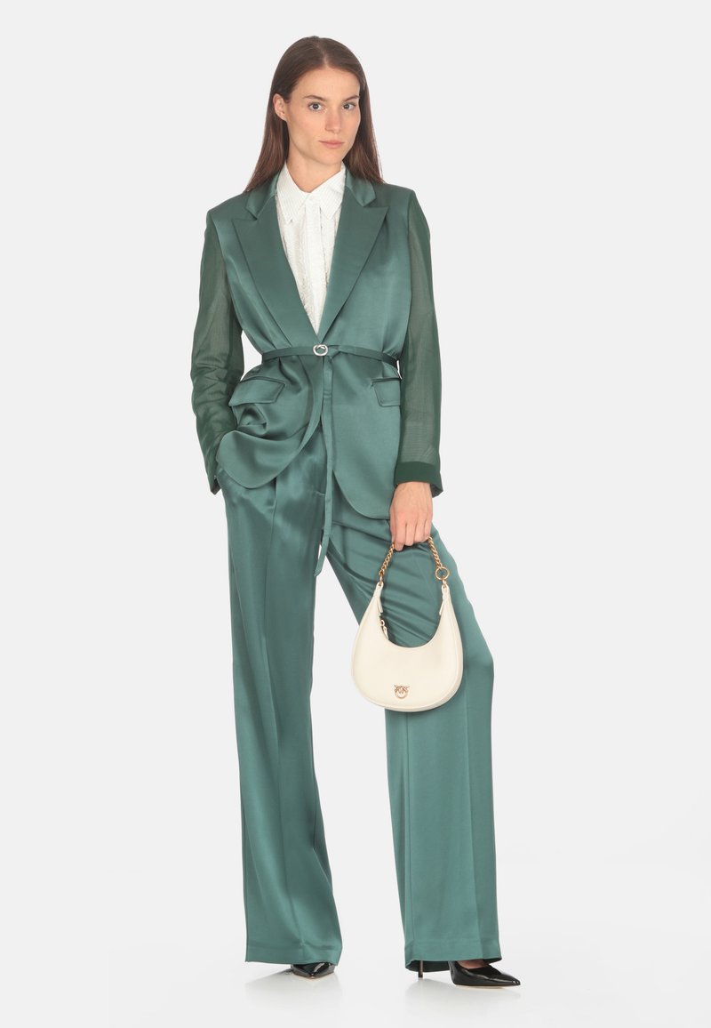 Costum verde din satin, bine croit, cu mâneci transparente, detaliu cu curea și două buzunare. Asortat cu o bluză albă și o geantă mică albă.