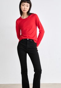 Κόκκινο πλεκτό πουλόβερ με μακριά μανίκια, συνδυασμένο με μαύρο τζιν υψηλής μέσης. Το πουλόβερ έχει στρογγυλή λαιμόκοψη, ενώ το τζιν διαθέτει μπροστινές τσέπες και εφαρμοστή γραμμή.