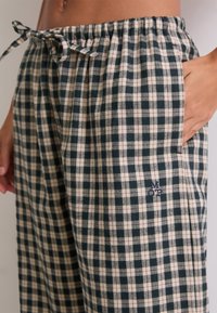 Close-up van een persoon in zwart-wit geruite broek met een trekkoord in de taille en hand in de zak.